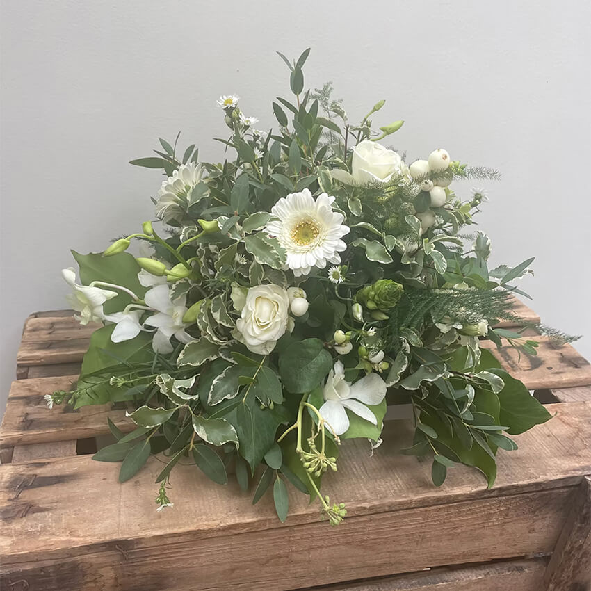 White arrangement of roses, gerbera, orchids and snowberries with variegated ivy on a wooden crate
