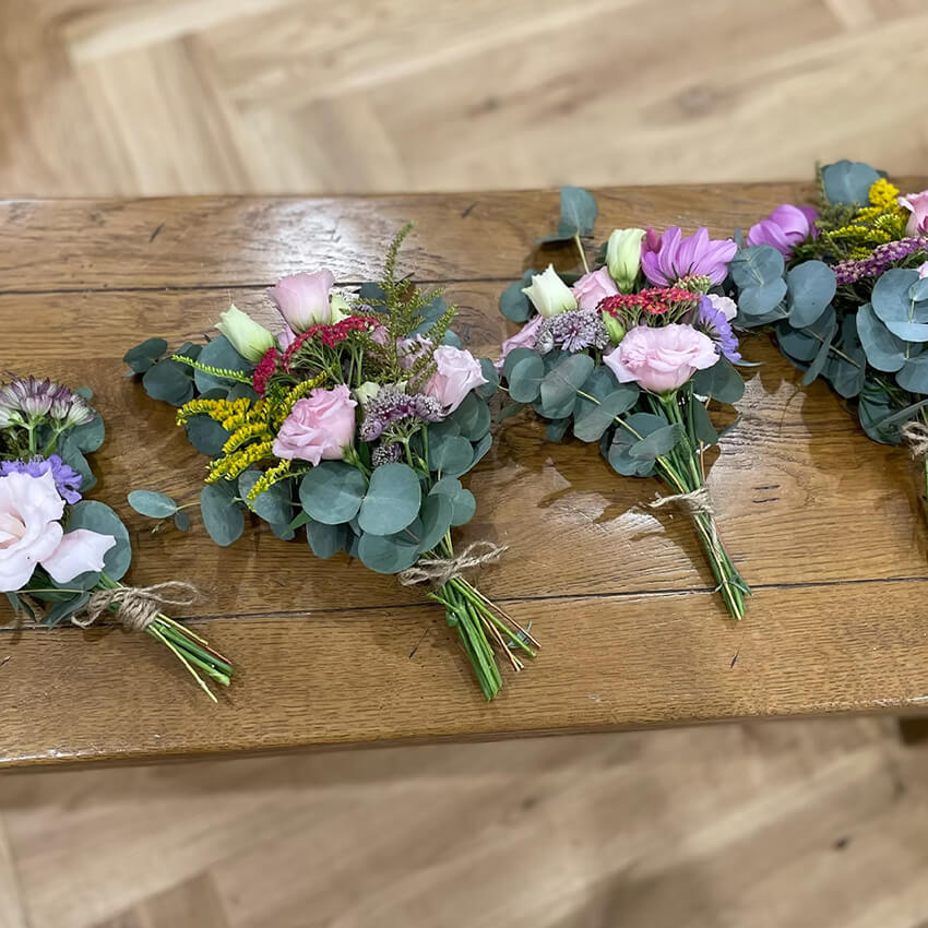 Wildflower buttonholes of pink lisianthus, purple scabiosa, yellow solidago and silver dollar eucalyptus tied with natural twine