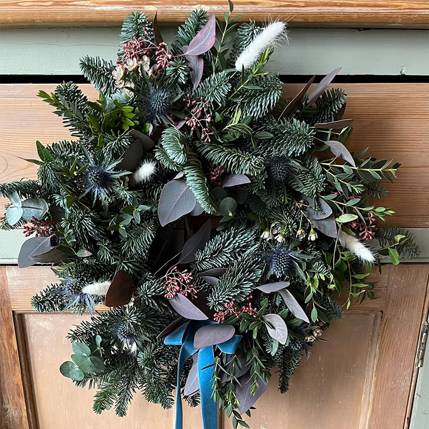Christmas door wreath of pine and fir with thistles, silver foliage, dried pampas and a blue velvet ribbon