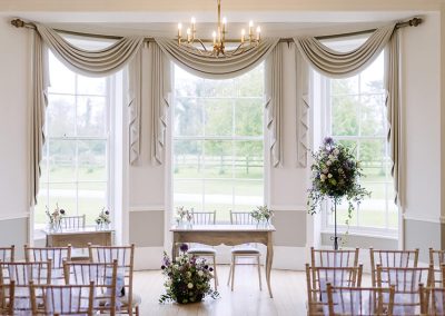 An elegant wedding ceremony room with wooden floors, tall windows and rows of chairs set ready for guests
