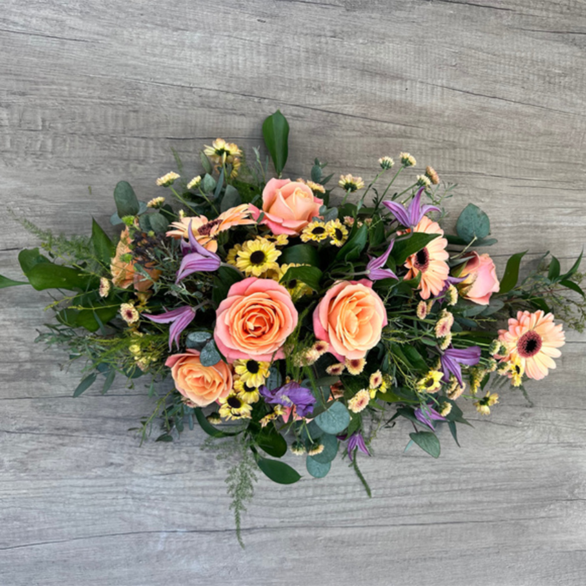 Elegant casket spray with peach-toned roses and wild garden blossoms