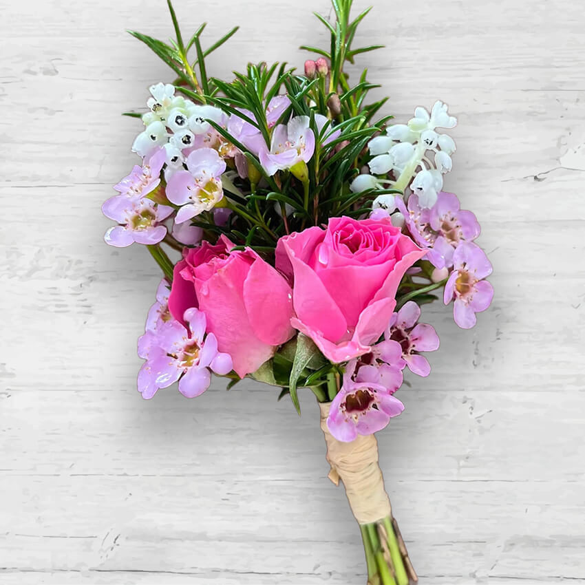 Pink rose and purple wildflower buttonhole sitting on a white wood background